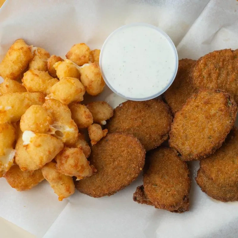 Fried cheese curds and pickles with dipping sauce in a container.