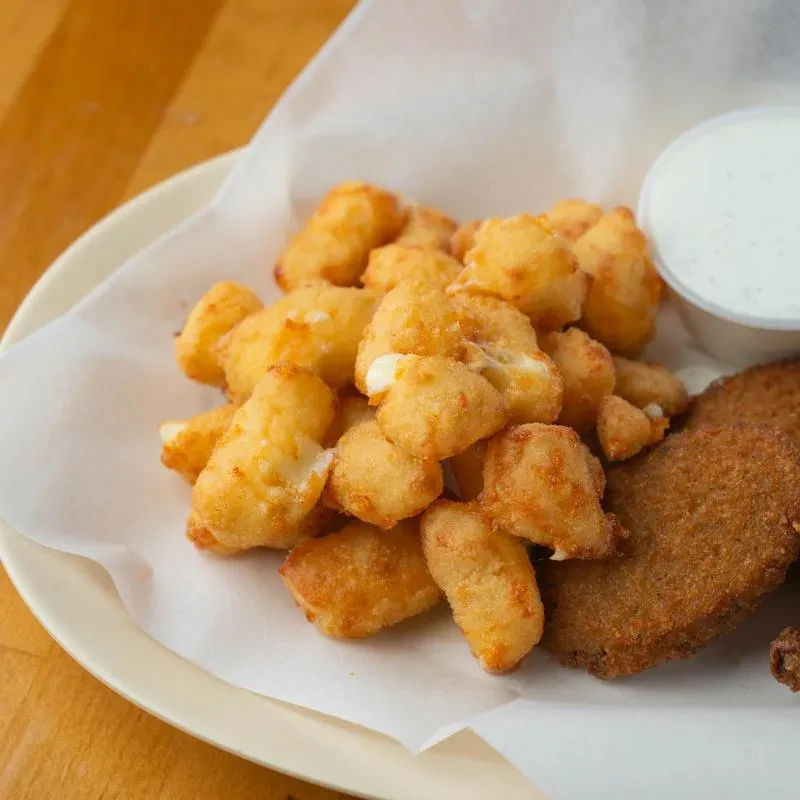 Golden fried cheese curds, dip, and other fried items on a plate.