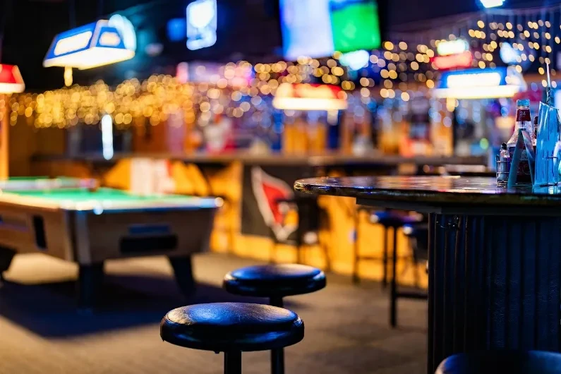 Empty bar interior with pool table, stools, and bokeh lights.