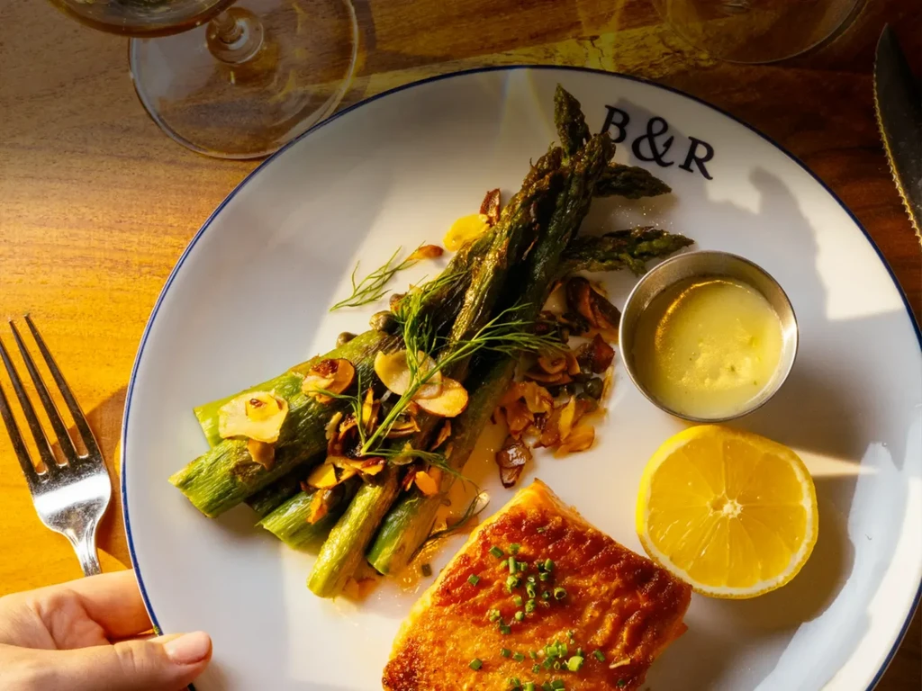 Plated grilled salmon, asparagus, lemon, and creamy sauce.