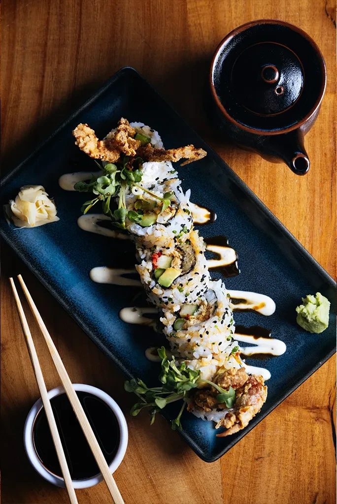 Tempura crab sushi roll with drizzled sauces, microgreens, chopsticks, ginger, wasabi.