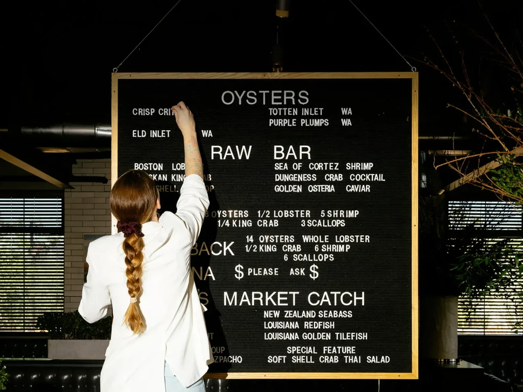 Woman adjusts a large black seafood menu board.