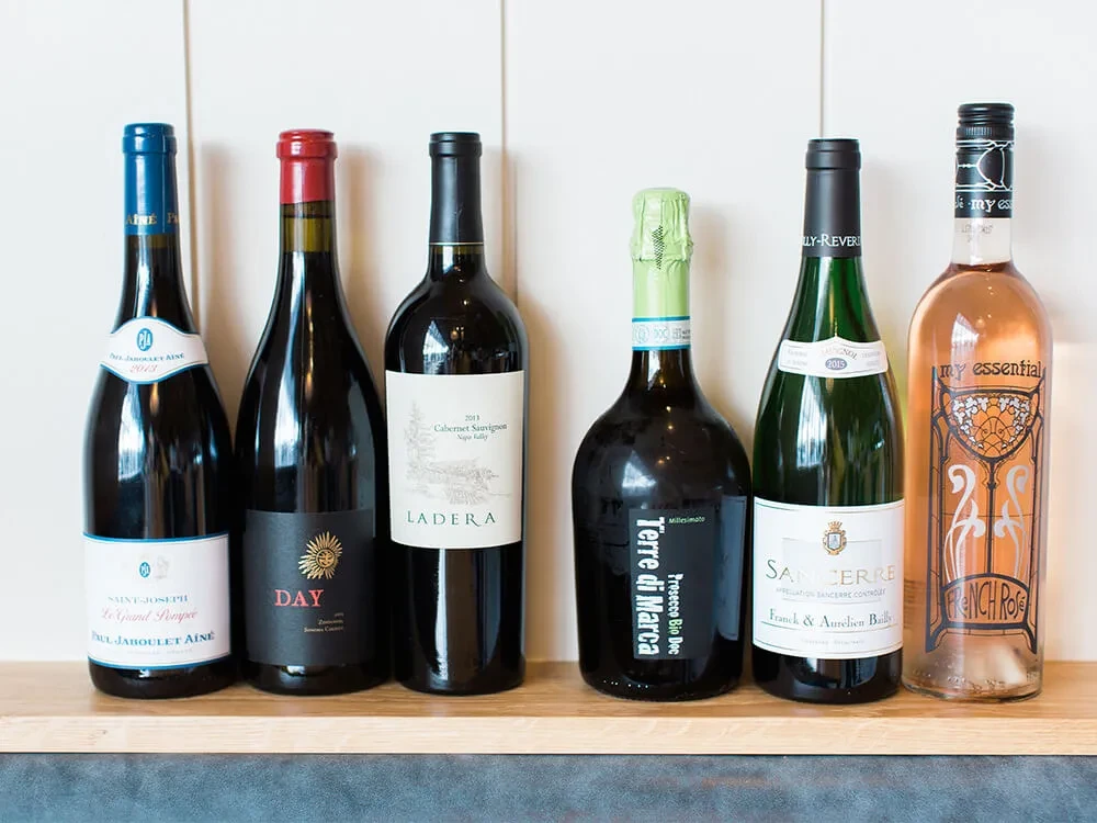 Six assorted bottles of wine and prosecco on a wooden shelf.