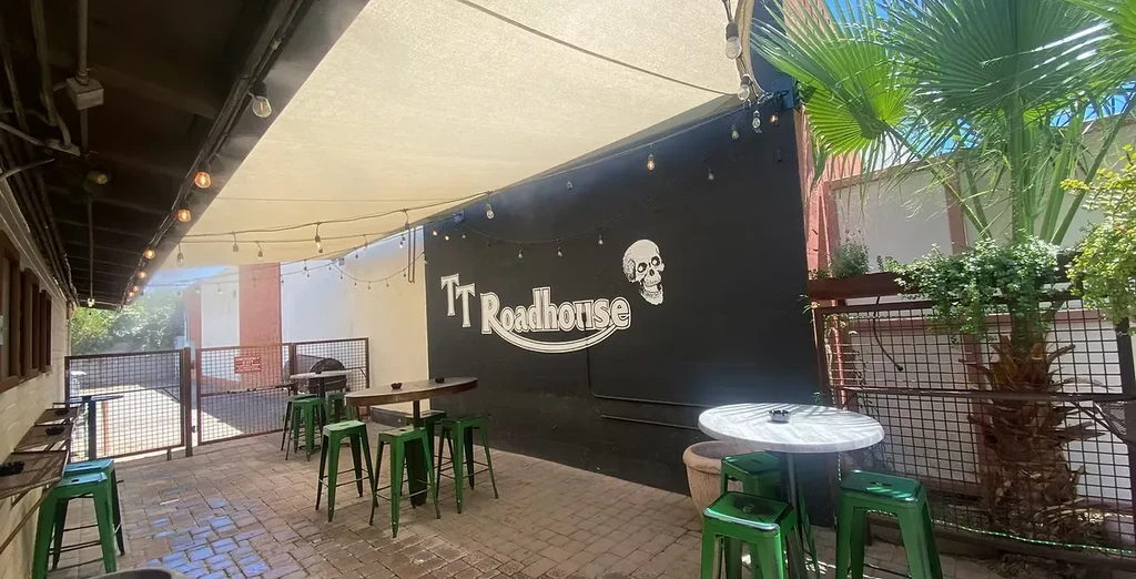Sunny TT Roadhouse patio with high-top tables, skull logo, and string lights.