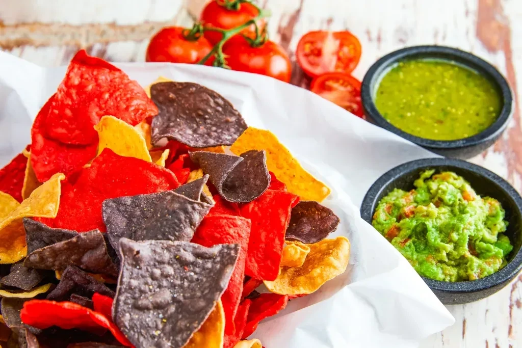 Colorful tortilla chips with salsa verde, guacamole, and fresh tomatoes.