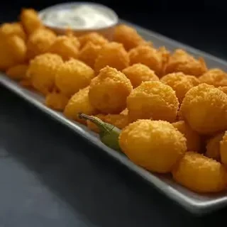 Platter of golden-brown fried appetizers, white dip, and a green chili.