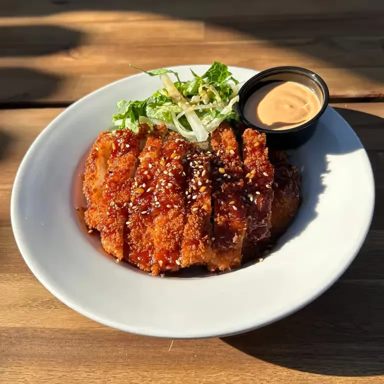 Fried cutlet, sliced, with sauce, sesame, green salad, and dip.