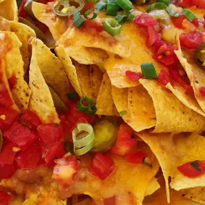 Vibrant loaded nachos with melted cheese, salsa, tomatoes, jalapeños.