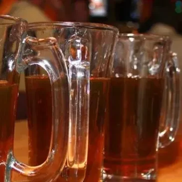 Lined-up glass mugs filled with dark amber liquid in a dim pub.