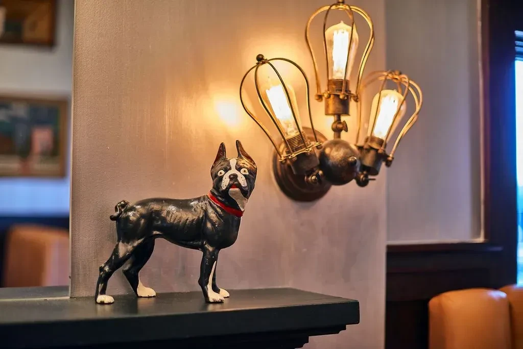Dark Boston Terrier statue with red collar and warm industrial caged lamp.