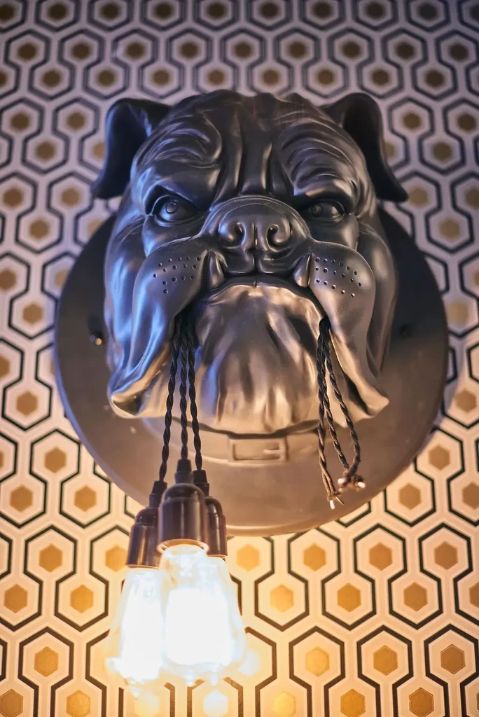 Dark bulldog head light fixture with three exposed bulbs and hexagonal wallpaper.