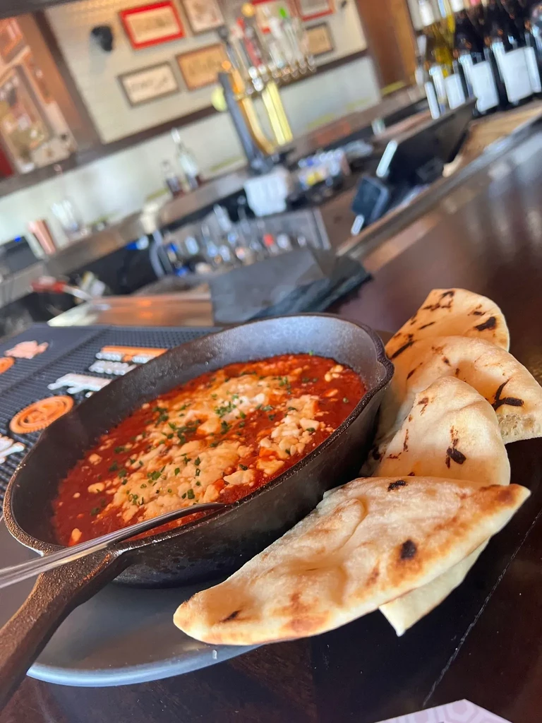 Red sauce and melted cheese skillet with flatbread on a bar.