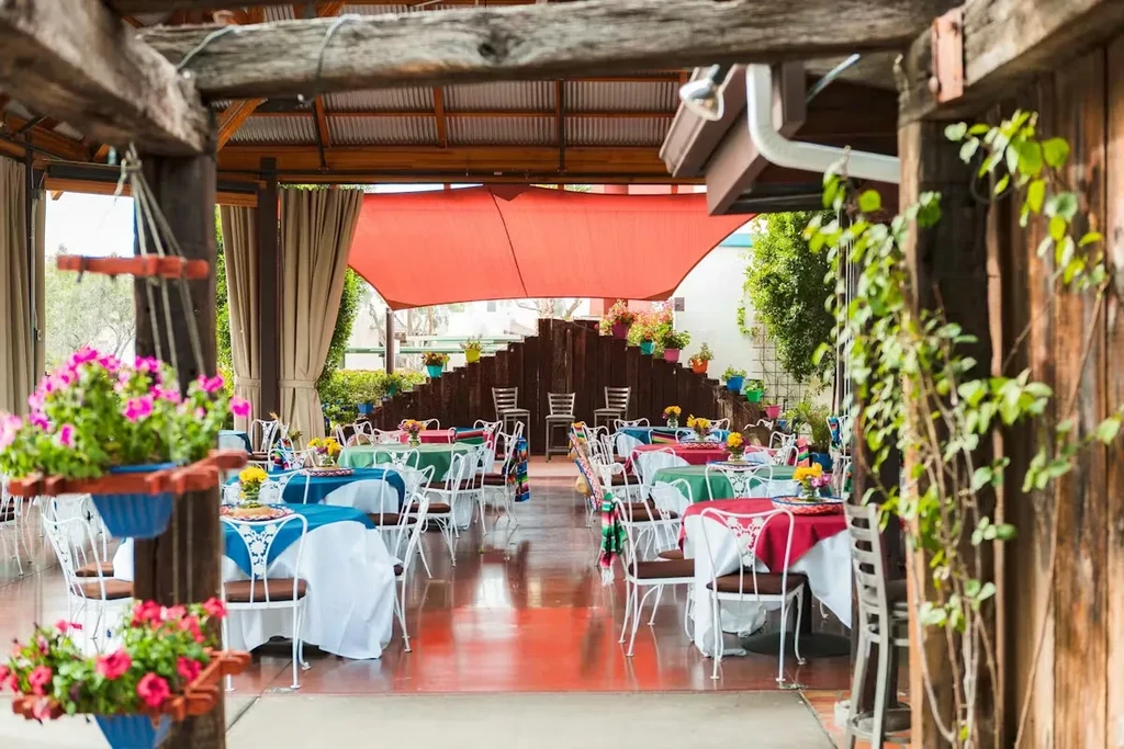 Empty outdoor patio with colorful tables, white chairs, and pink flowers.
