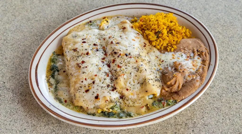 Creamy enchiladas, yellow rice, and refried beans on an oval plate.