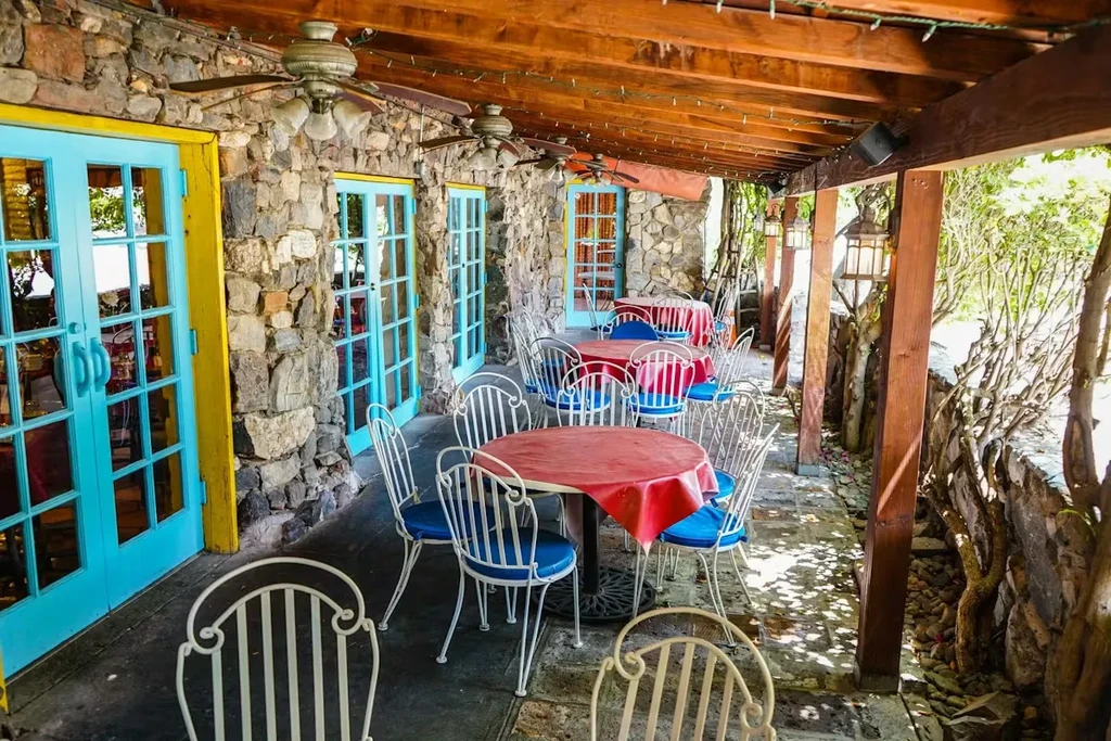 Covered outdoor patio with stone walls, turquoise doors, red tables.