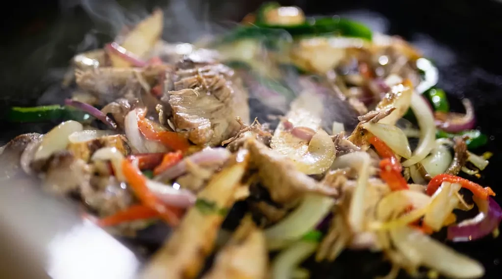 Steaming shredded meat and vibrant vegetables cooking on a hot surface.