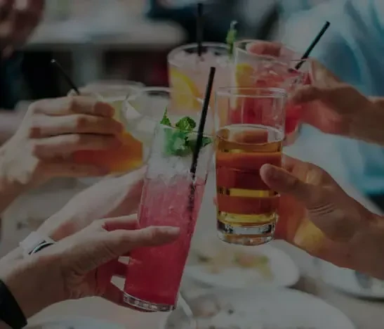 Group of hands toasting with assorted colorful cocktails and a beer.