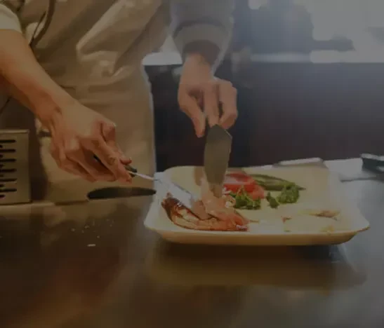 Hands plating cooked seafood and vegetables with tongs and spatula.