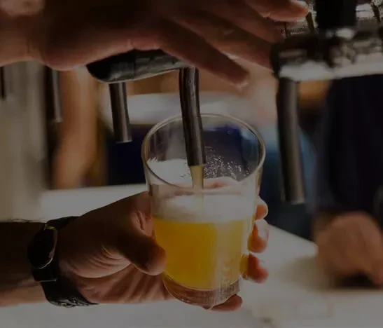 Hands pouring beer from a tap into a glass.