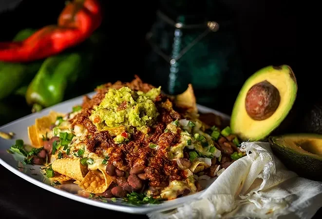 Loaded nachos with guacamole, meat, cheese, beans, and avocado.