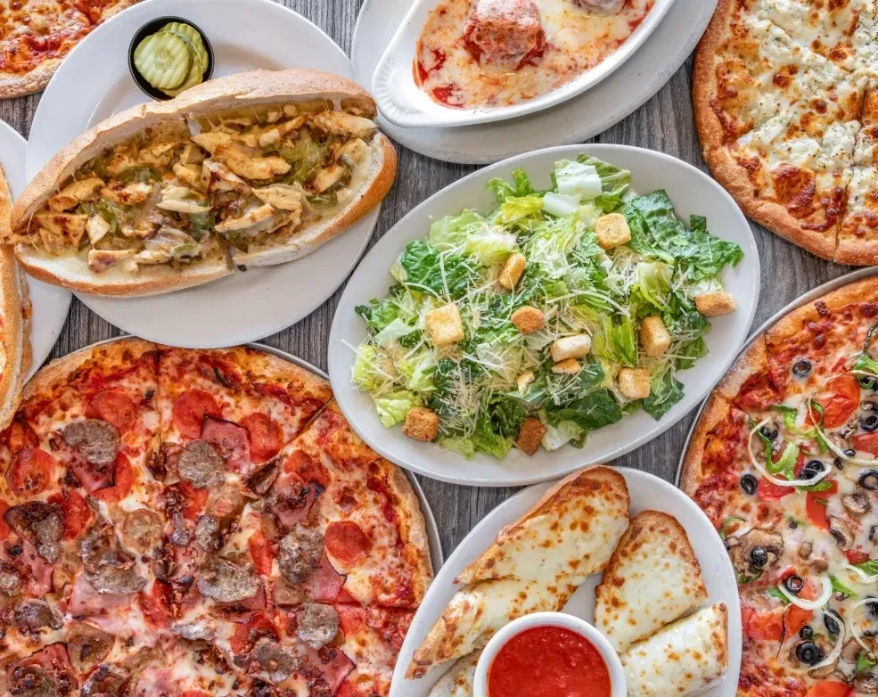 Italian-American food spread: multiple pizzas, hoagie, meatballs, and Caesar salad.
