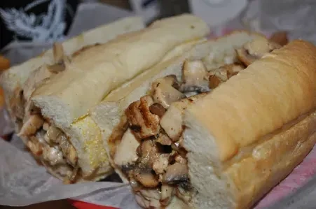 Sliced chicken and mushroom sub on white bread, on paper.
