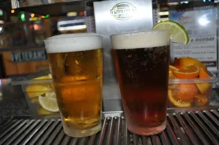 Light and dark beer glasses on a drip tray with fruit garnishes.
