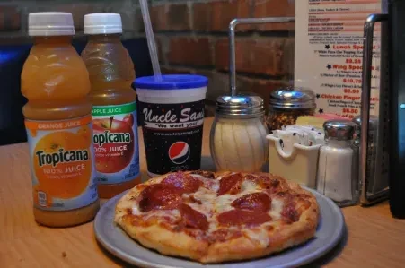 Close-up of a pepperoni pizza, juices, and condiments on a wooden table.