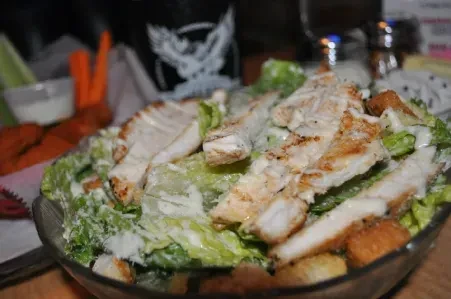Grilled chicken Caesar salad served in a clear glass bowl.