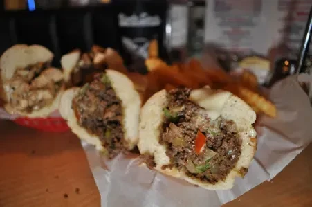 Cheesesteak sandwiches, cut in half, with meat, cheese, peppers, and blurry fries.