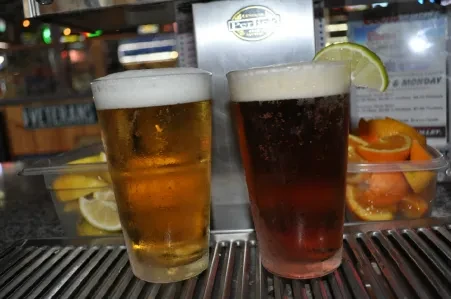 Two cold beers, amber and dark with lime, on a bar.
