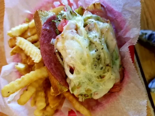 Close-up of cheesy hot sub sandwich with meat, vegetables, and fries.