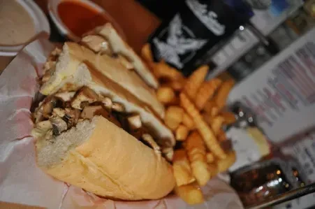 Close-up of a meat and mushroom sub sandwich with crinkle-cut fries.
