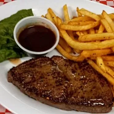 Seared steak, golden fries, sauce, and lettuce on a checkered table.