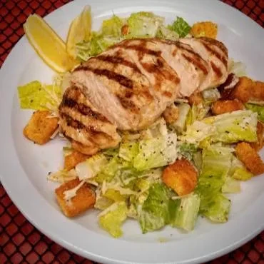 Overhead Caesar salad with char-marked grilled chicken and lemon wedges.