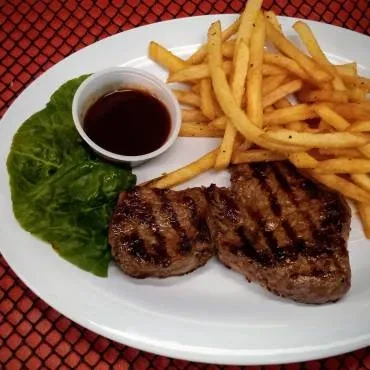 Two grilled steaks, french fries, lettuce, and dark sauce.
