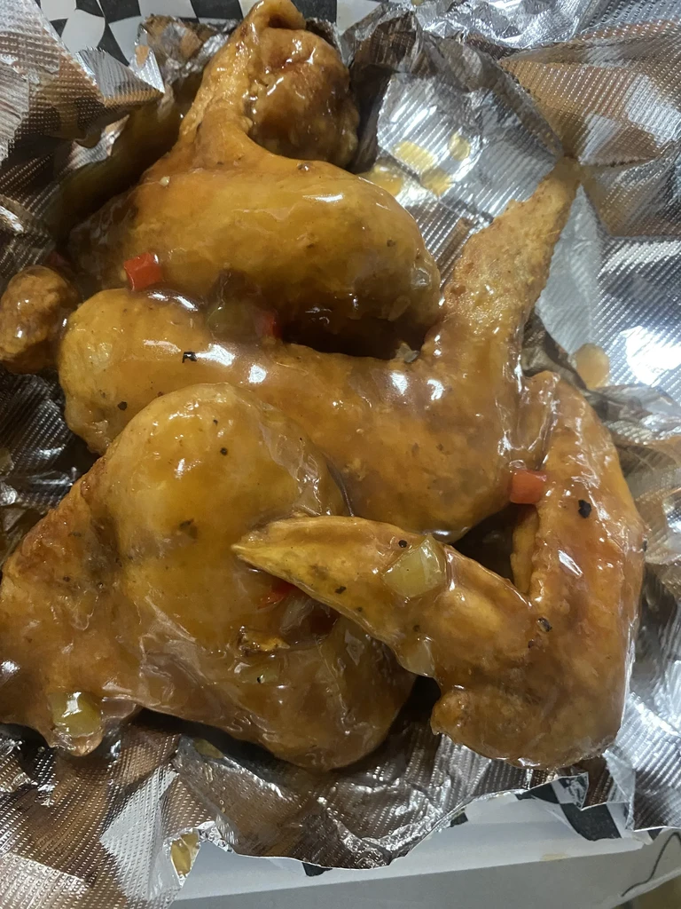 Chicken wings in amber sauce with bell peppers in a takeout box.