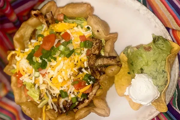 Taco salad bowl with chicken, guacamole, sour cream, on a striped blanket.