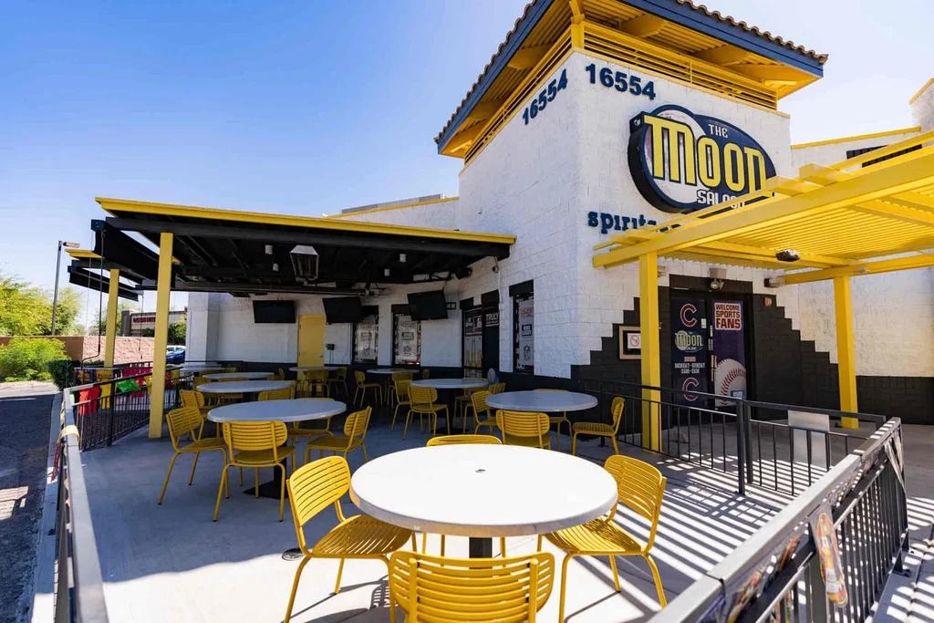 Sunny patio of The Moon Saloon with yellow chairs and TVs.