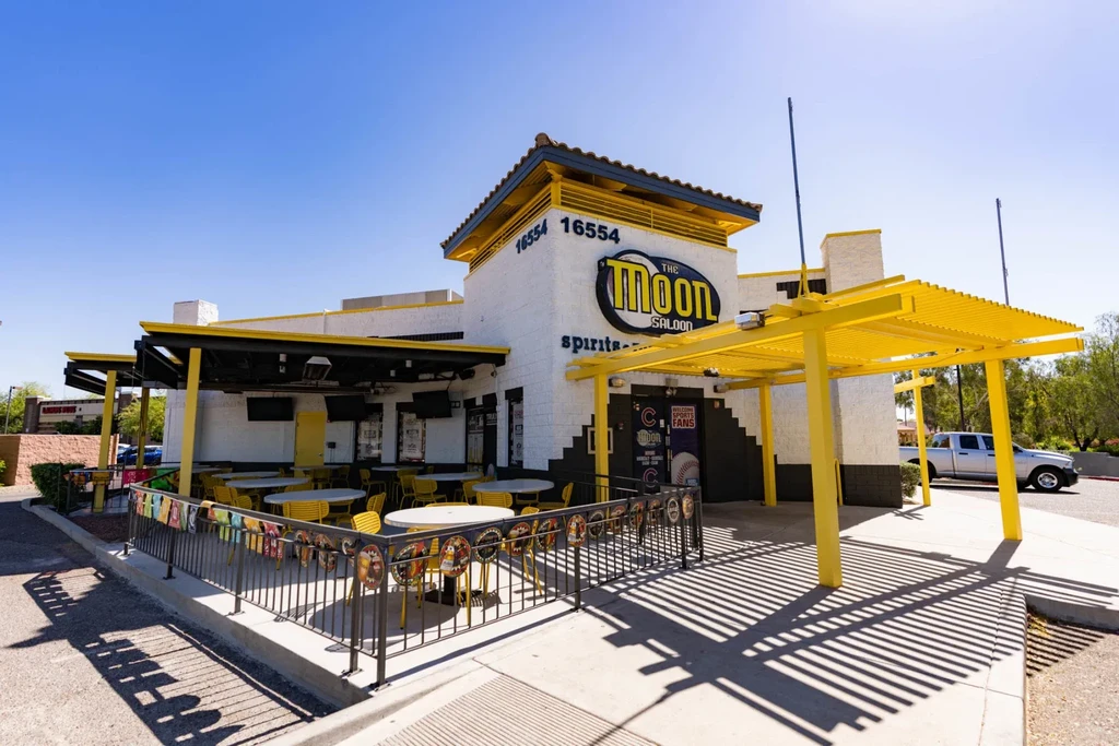 The Moon Saloon exterior: white building with yellow accents and patio.