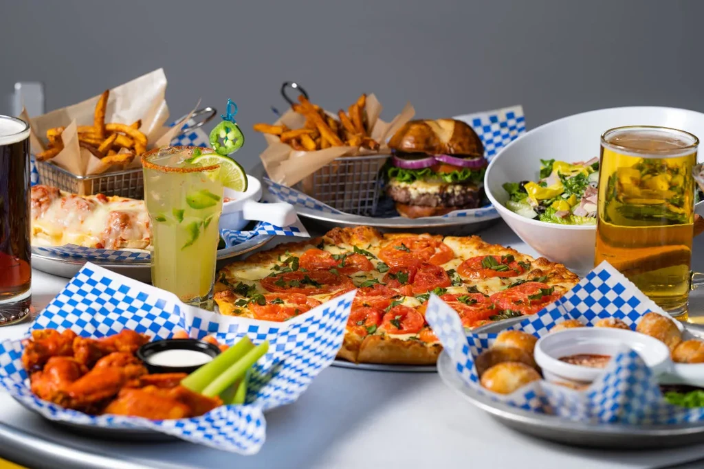 Casual dining spread: pizza, wings, burger, fries, salad, beer, cocktail.