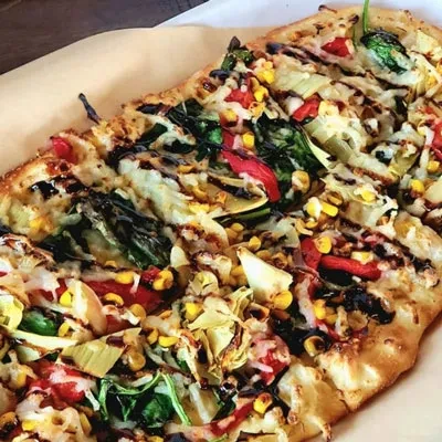 Rectangular flatbread pizza with corn, peppers, artichoke, cheese, balsamic drizzle.