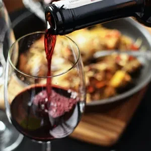 Red wine poured into a glass, roasted chicken in blurred background.