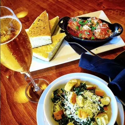 Meal of focaccia, meatballs, salad, and sparkling drink on a wooden table.