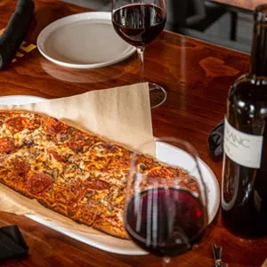 Rectangular pepperoni, sausage flatbread pizza served with red wine.