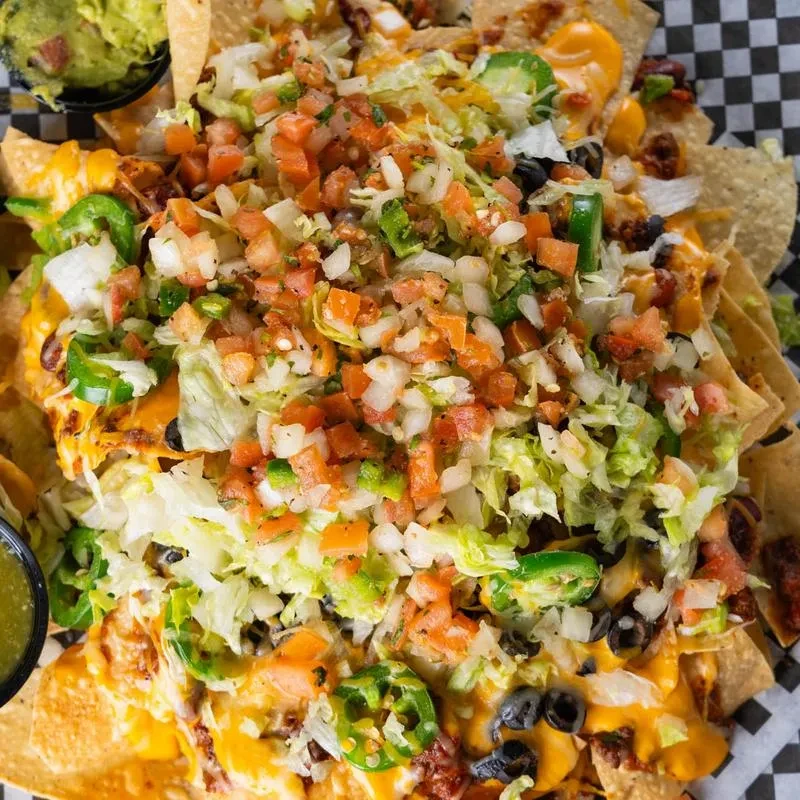Top-down view of loaded nachos with cheese, meat, fresh veggies, guacamole.