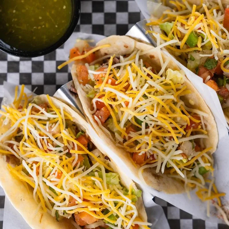 Three tacos with meat, cheese, lettuce, salsa, on checkered surface.
