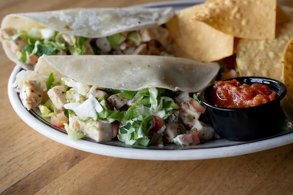 Close-up of two chicken tacos, chips, and salsa on a wooden table.
