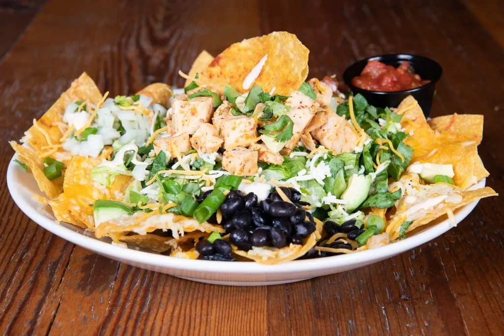Large plate of chicken nachos with cheese, lettuce, avocado, and salsa.