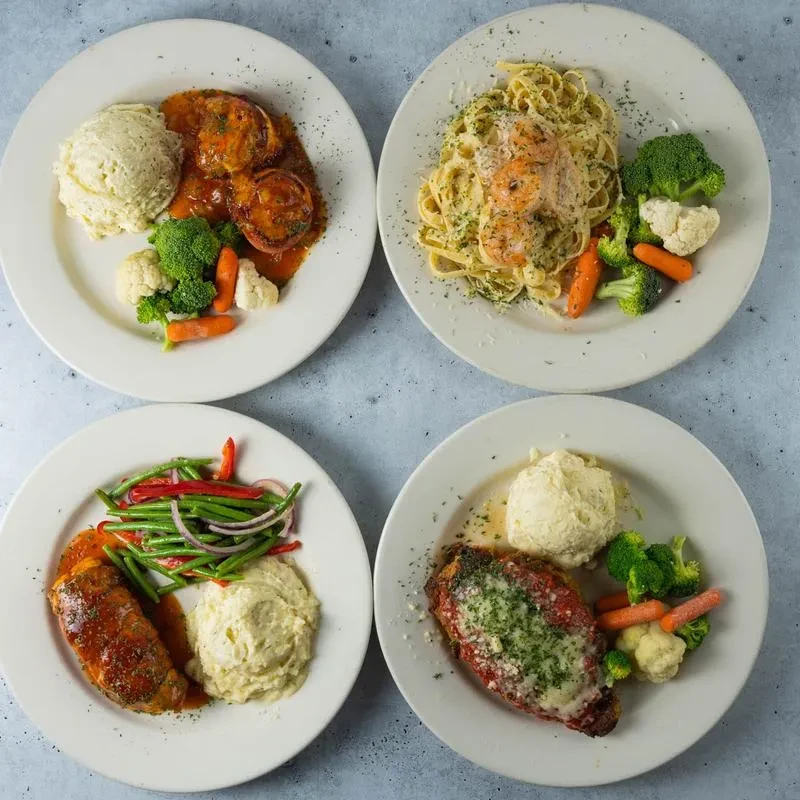Four distinct cooked meals on white plates, arranged in a grid.